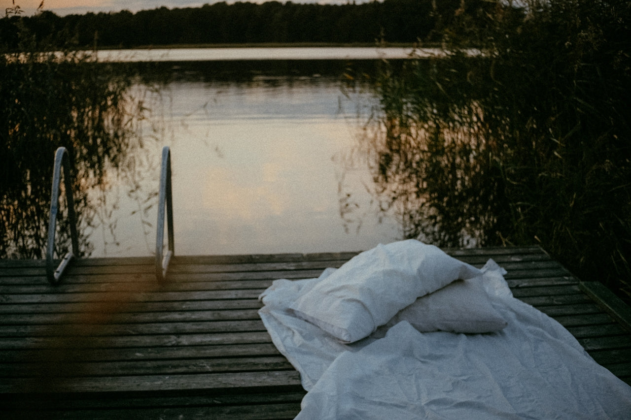 Peaceful lakeside sleep setup with white bedding on a wooden dock at sunset – natural sleep environment for better rest and relaxation
