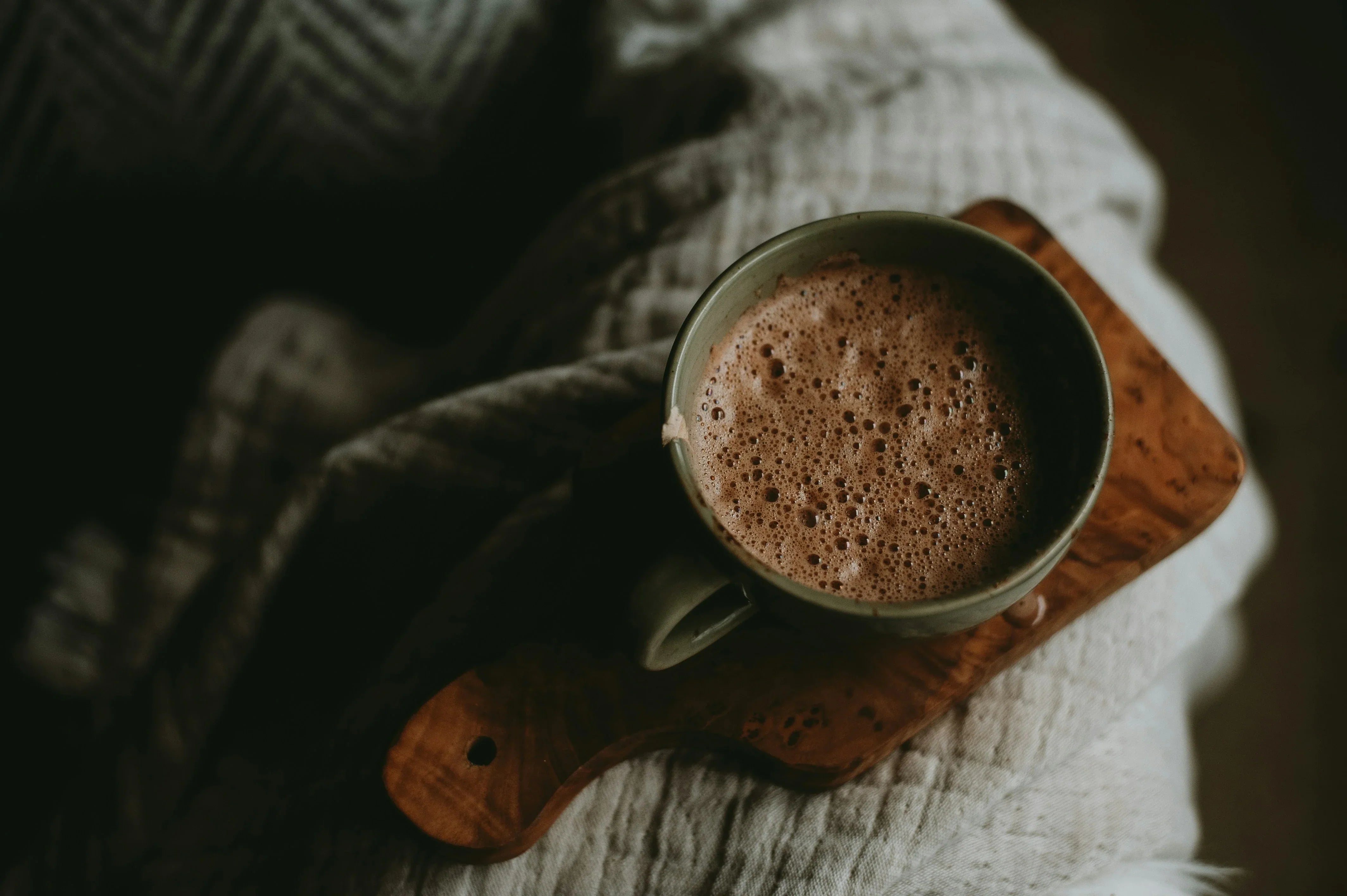 A cozy mug of frothy mushroom cocoa resting on a wooden board