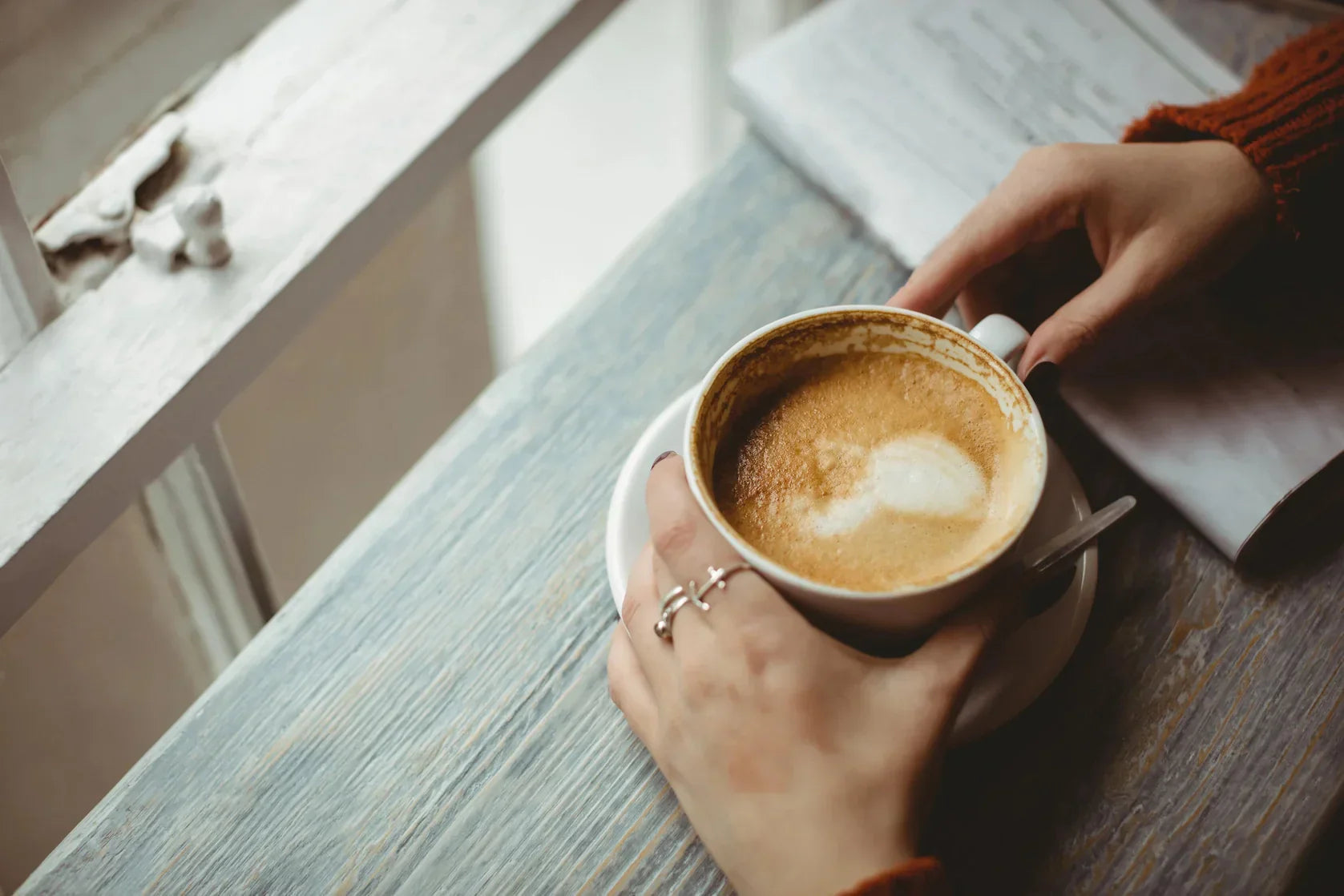 A person holding a cup of coffee on a wooden table.