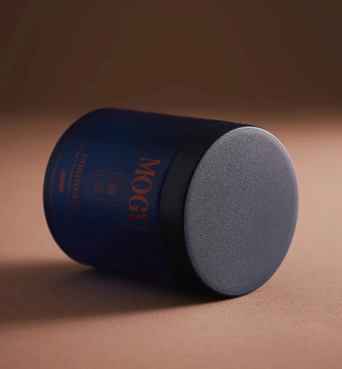 Cordyceps capsules in a blue cylindrical container with gray lid on a brown background