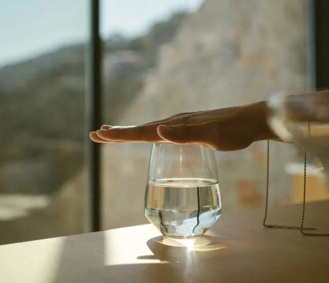 Minimalist scene of a hand over a glass of water in sunlight, symbolizing mental clarity and hydration—visual concept for mindfulness and cognitive support through natural supplements.