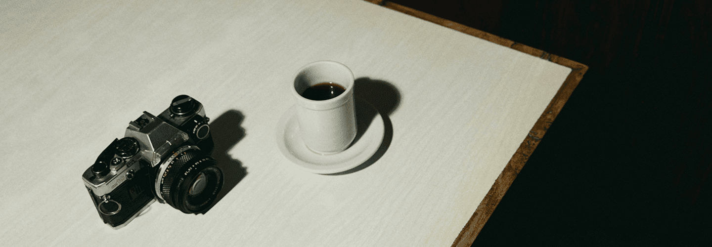 Minimalist still life with a cup of mushroom coffee and vintage camera on a white table.