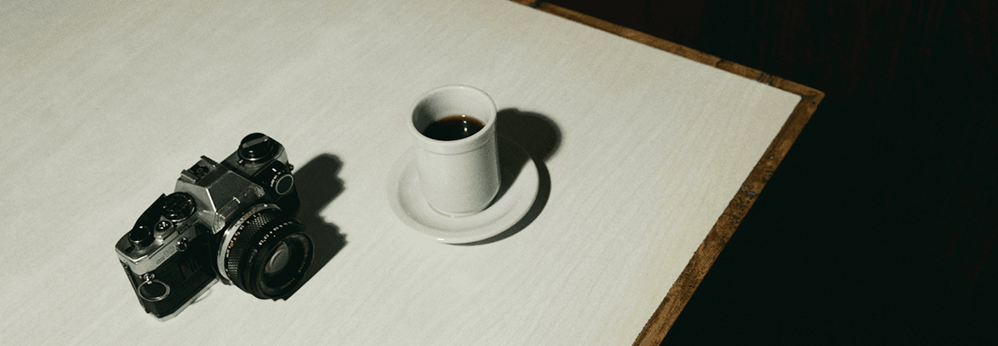 Minimalist still life with a cup of mushroom coffee and vintage camera on a white table.