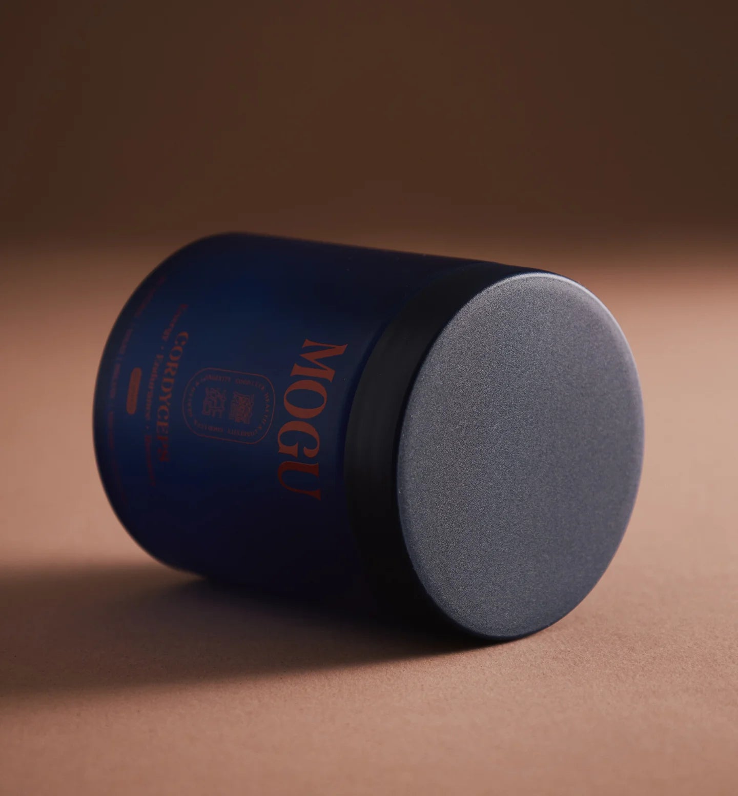 Cordyceps capsules in a blue cylindrical container with gray lid on a brown background