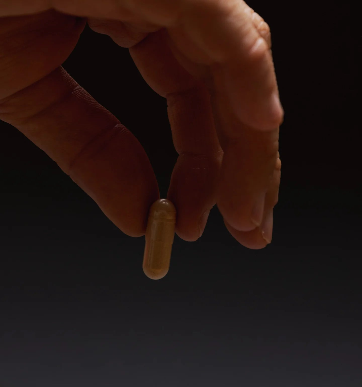 Hand holding a Reishi capsule against a dark background