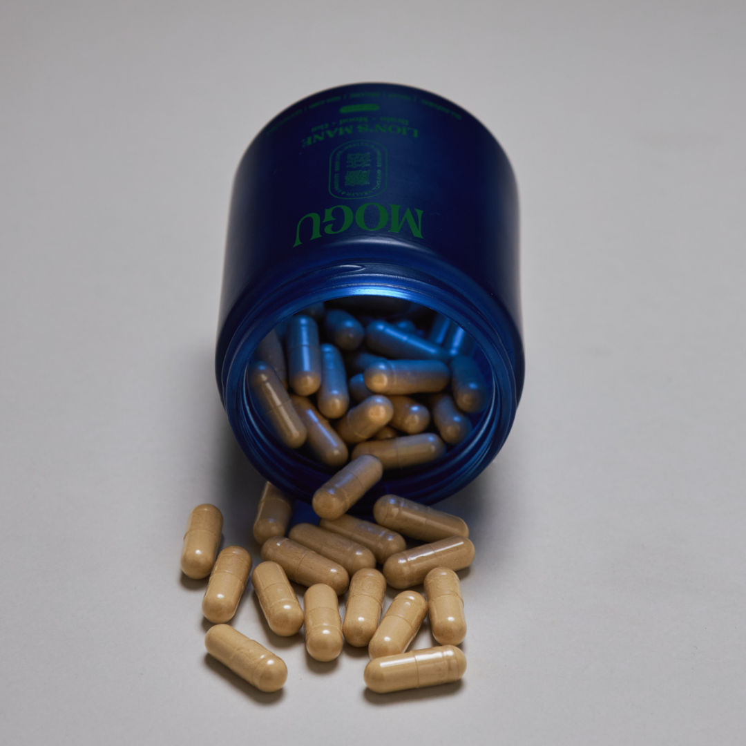 MOGU capsules in a blue container with 'MOGU' branding, partially open, revealing brown capsules on a gray background.